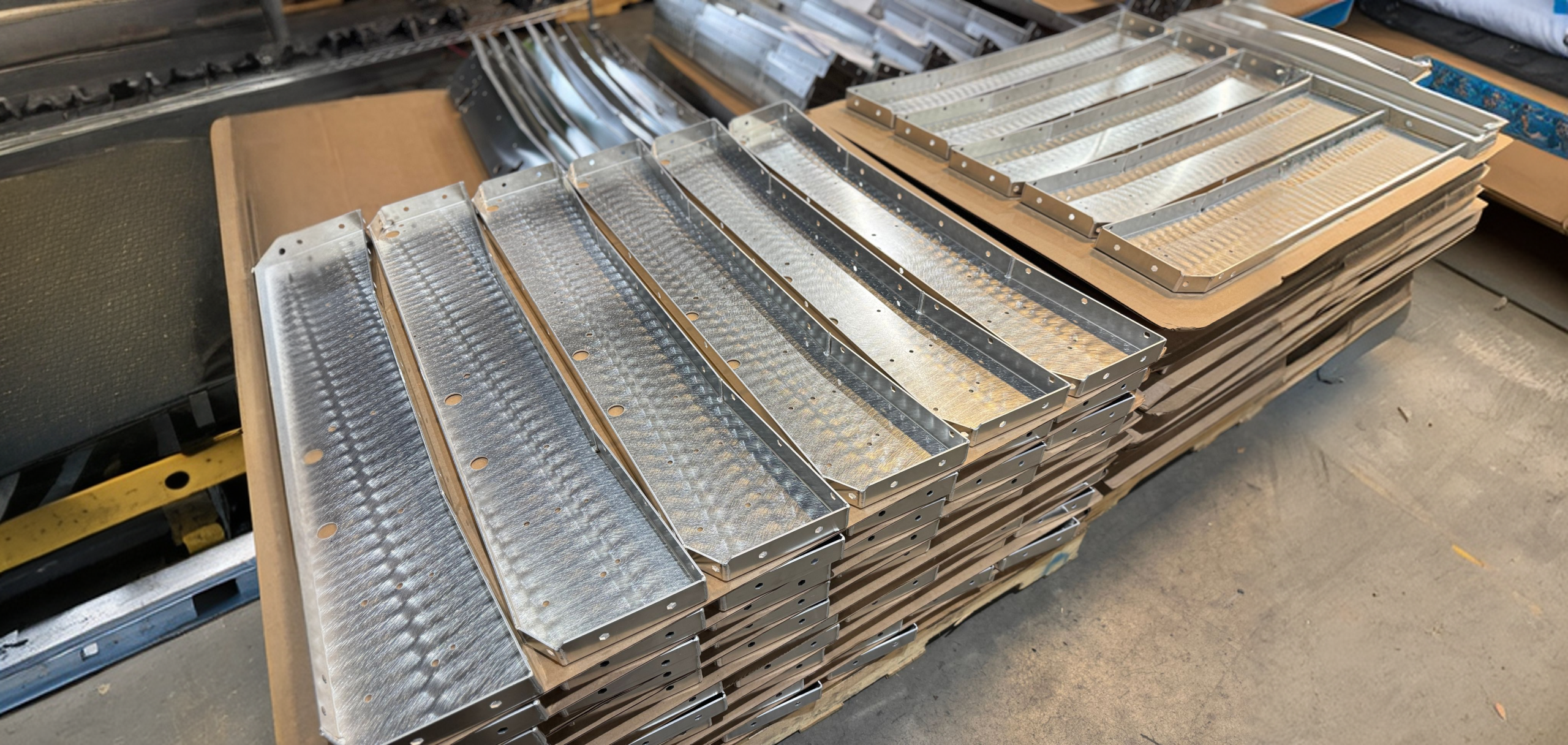 Stacks of metal grating panels and curved strips stored on pallets in a workshop.
