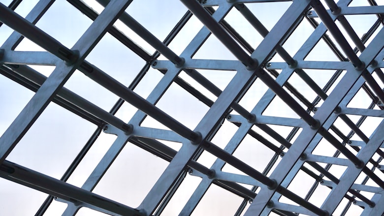 Abstract intersecting steel beams forming a geometric lattice against a bright sky.