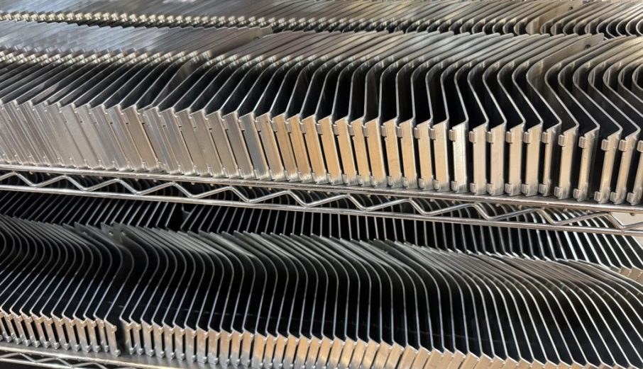 Rows of black and beige metal parts stacked on wire shelving in a workshop.