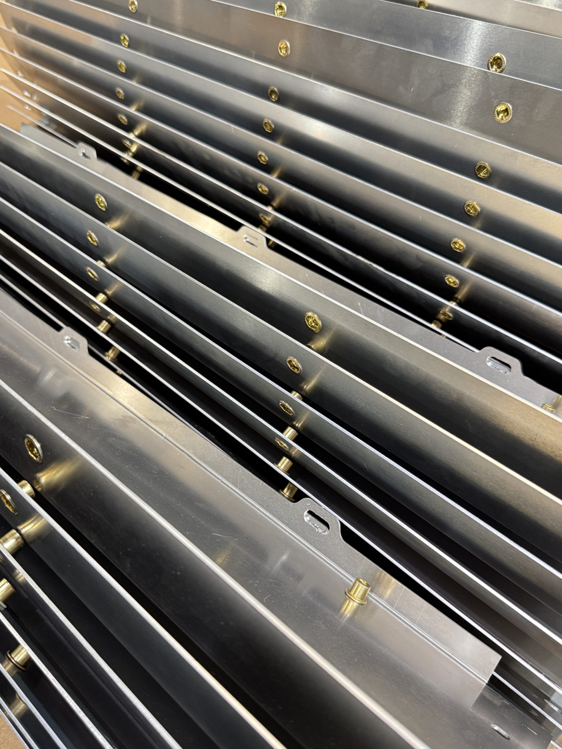 Stacked metal panels with rows of gold fasteners in a workshop setting.