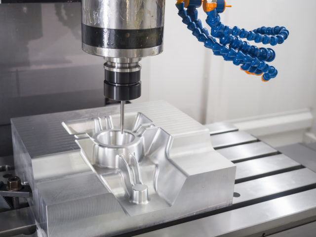 CNC milling machine machining a shiny aluminum block with a drill bit over a metal workpiece.