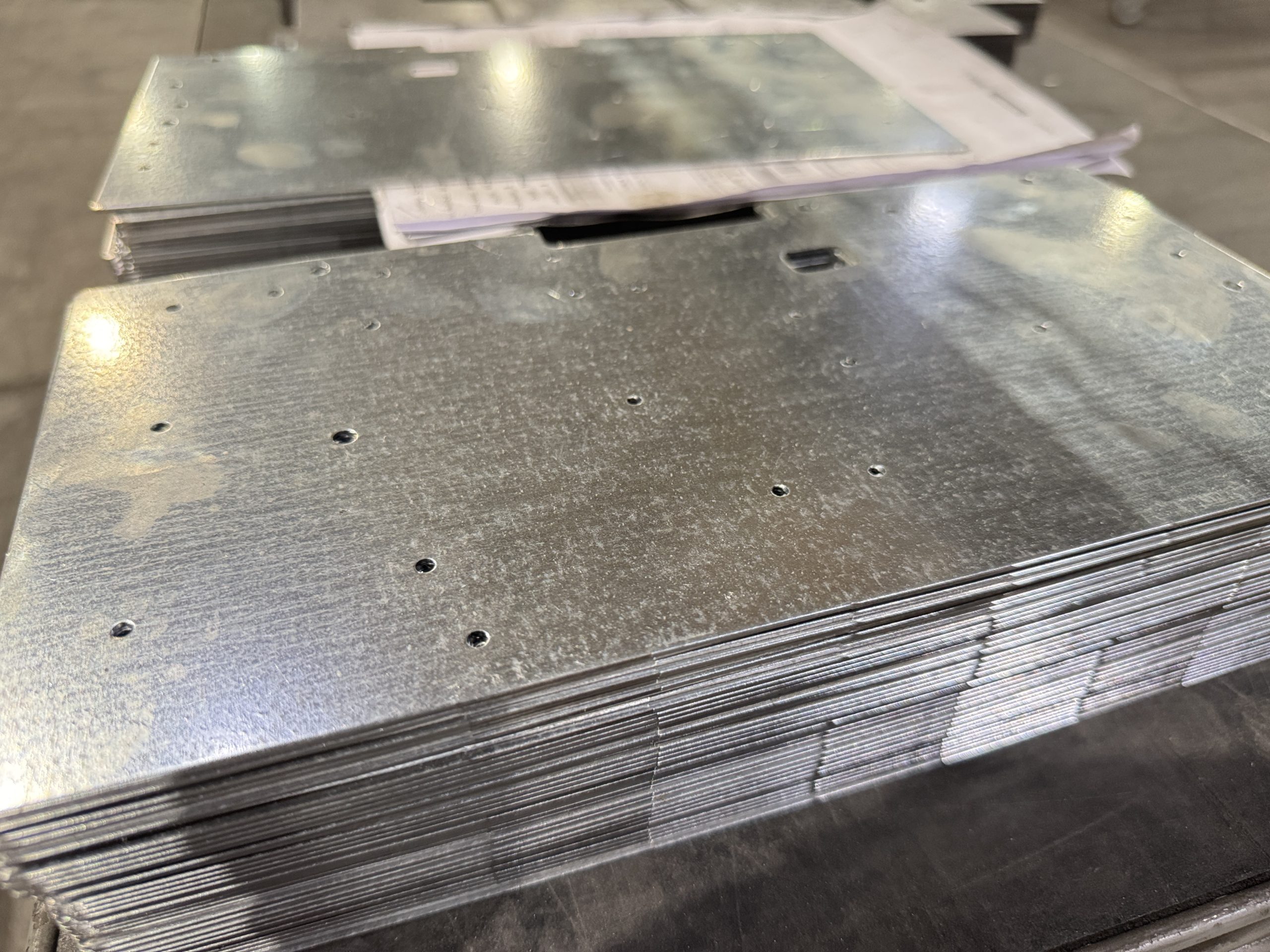 Stacked galvanized metal sheets with punched holes on a workbench.