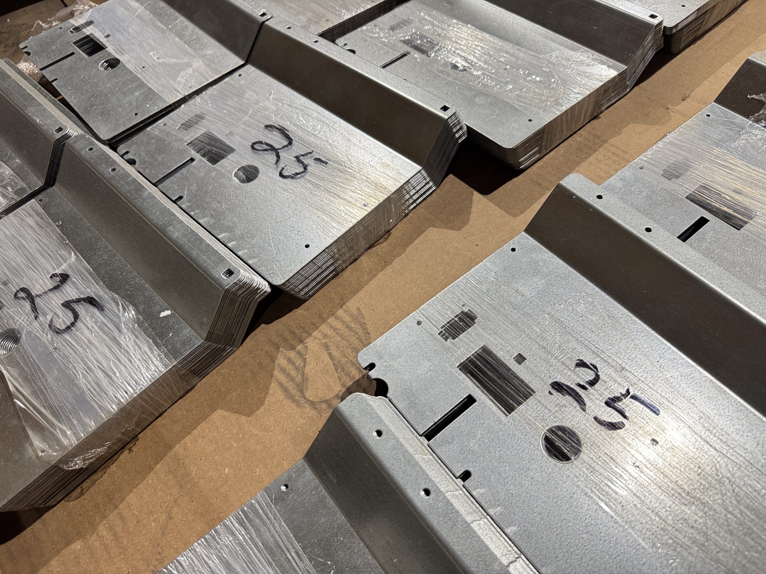 Stacked metal parts marked with handwritten numbers on a cardboard surface.