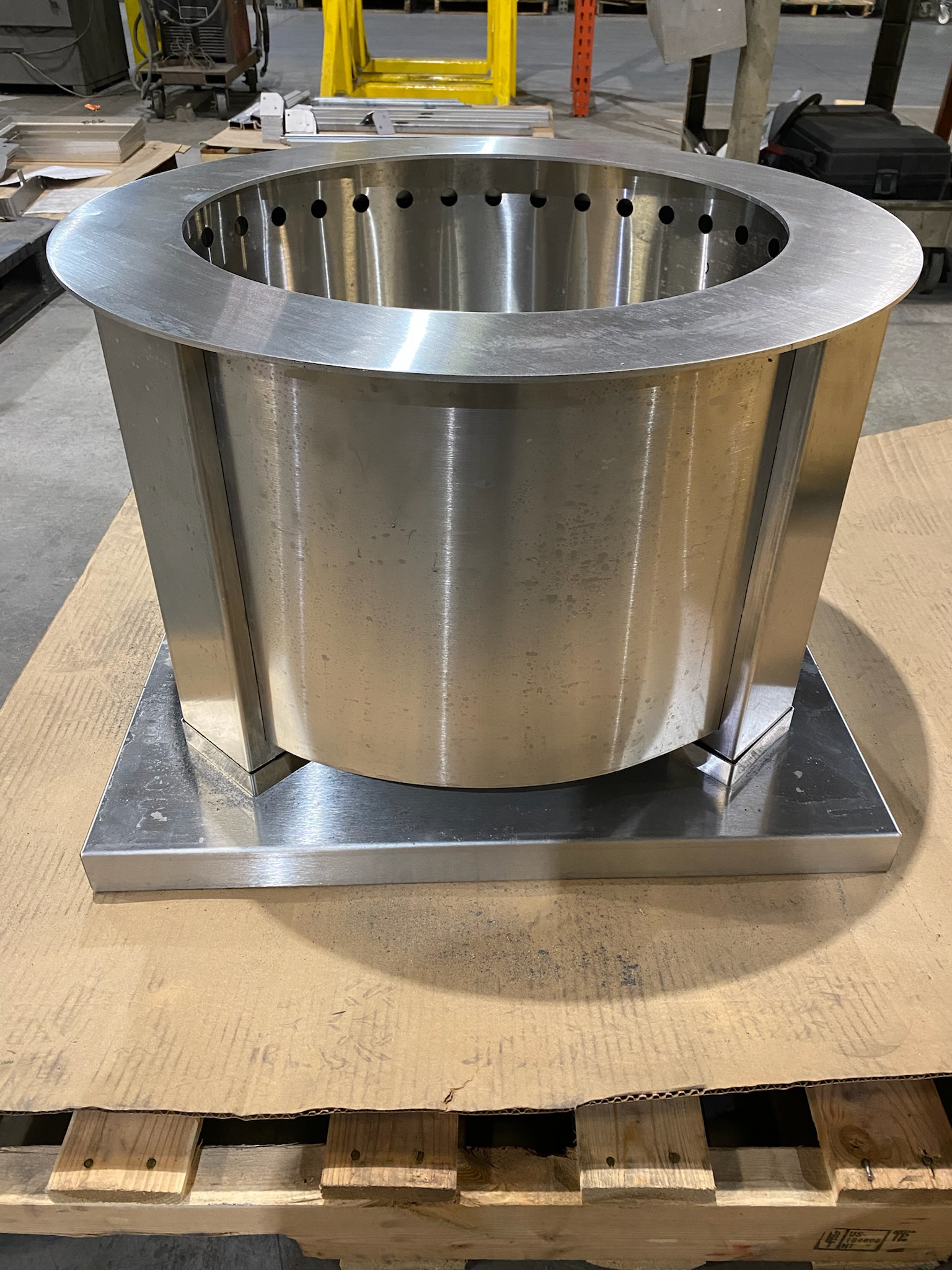 Large stainless steel cylindrical metal component on a pallet in an industrial workshop.