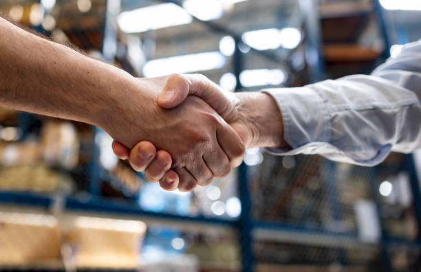 Two people shake hands in a warehouse or industrial setting.