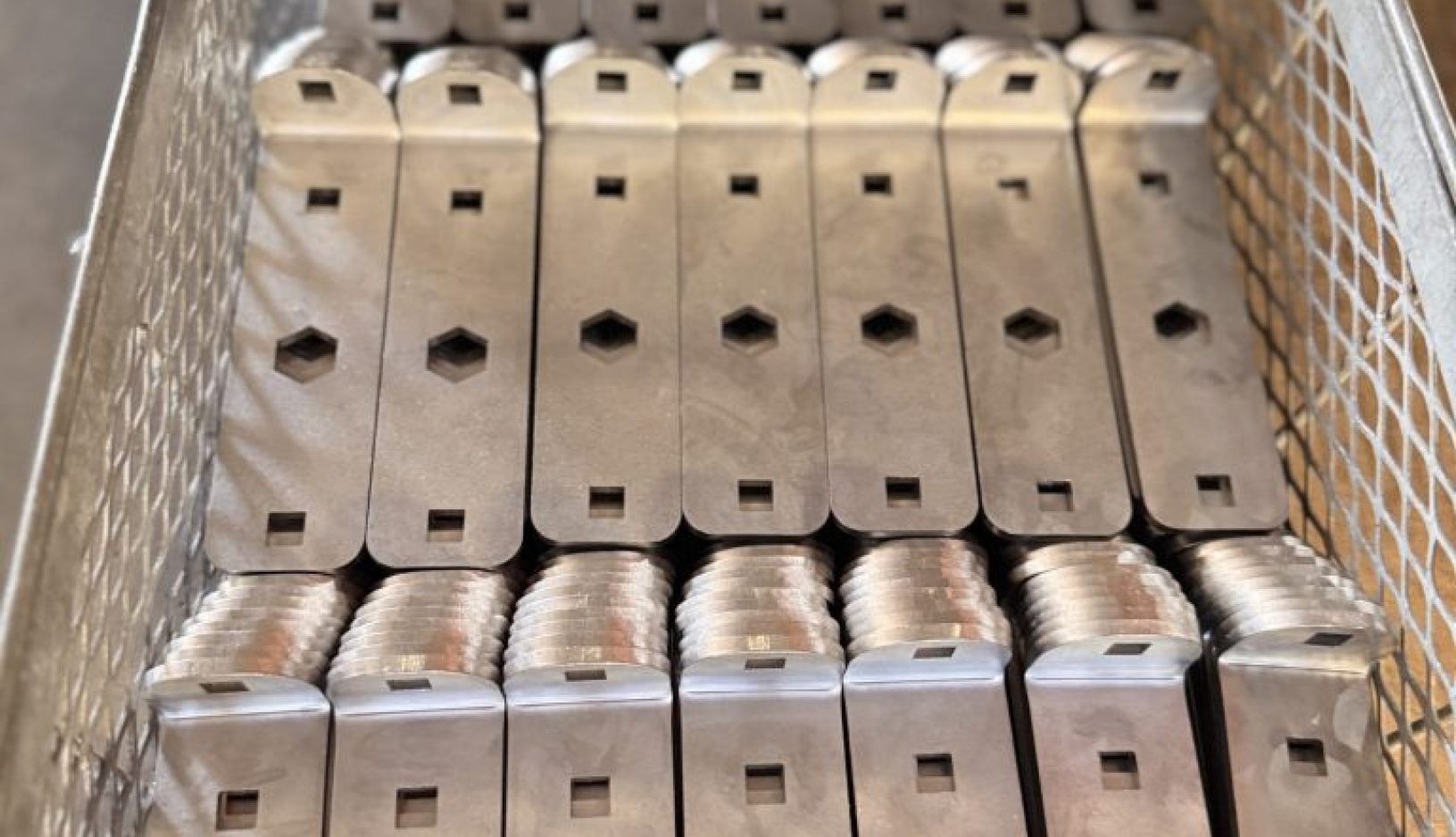 Metal trays stacked inside a wire basket with a repeating industrial pattern.