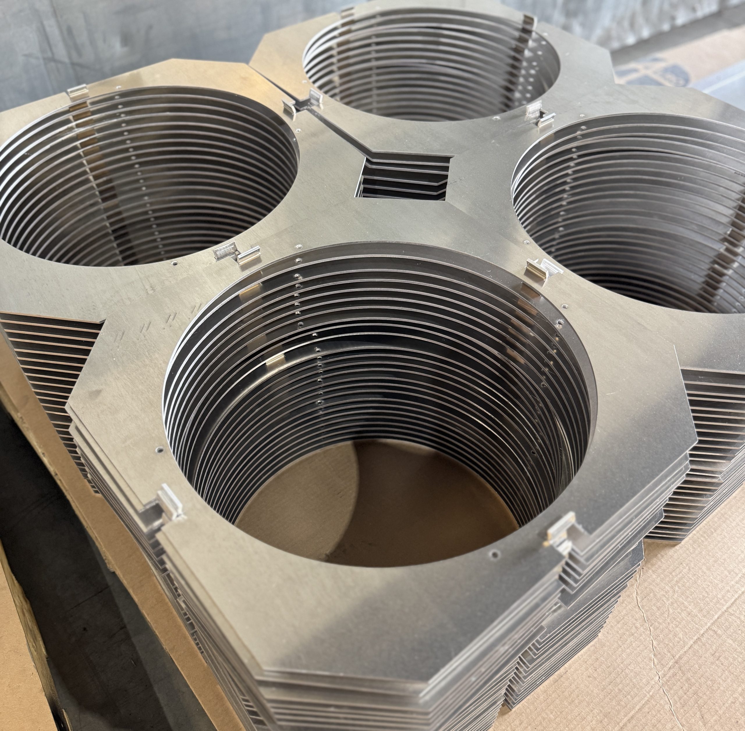 Stacked hexagonal metal plates with large circular cutouts arranged on a work surface.